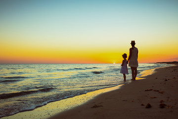 mother and daughter travellers standing on seashore at sunset