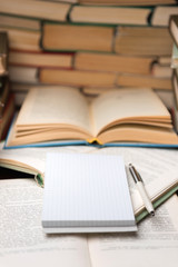 Education learning concept with open book and notebook on the table. Stack piles of books on reading desk and glasses in bookshelves background