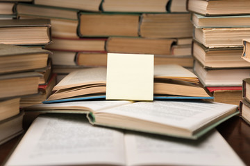 Education learning concept with open book and notebook on the table. Stack piles of books on reading desk and glasses in bookshelves background