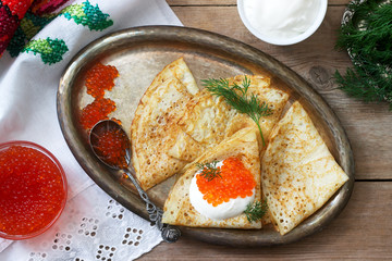 Homemade pancakes with red caviar, sour cream and dill served with vodka. Rustic style.