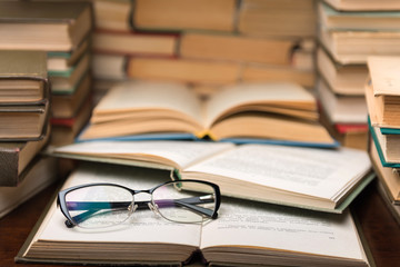 Open book and glasses on wood desk in the library room with blurred focus for education background and back to school concept