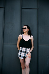 Sexy girl near a dark wall in a T-shirt, sunglasses and short shorts