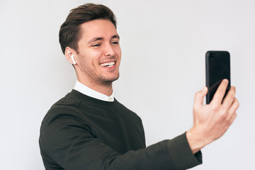 Happy man smiling and standing isolated on white studio background, looking at screen of cellphone and talking self portrait, browsing web pages and smiling nicely while chatting with friends.