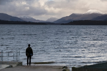 Fototapeta na wymiar Lonely man in wild landscape mountains and lake in winter storm clouds at Loch Lomond Scotland
