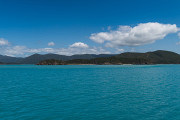 Inselblick in türkis-farbenem Wasser und blauem Himmel mit weißen Wolken