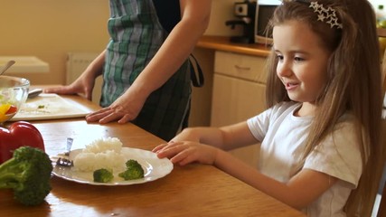 Little preschool brunette refuse to eat healthy food. Mom pushes her plate