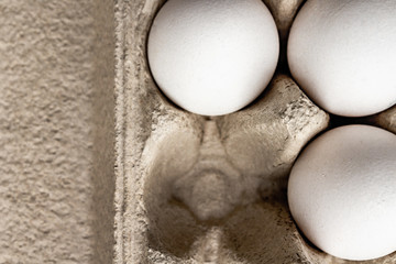 Three white chicken eggs in a paper grey box with copy space