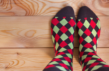 Two legs in multi-colored socks on a wooden floor. 
