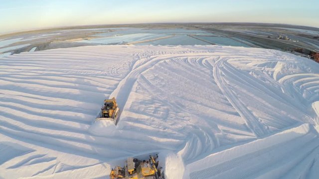 Aerial drone shot of tractors working on a large salt deposit in the salt flats by solar evaporation in Guerrero Negro, Ojo de Liebre lagoon, Biosphere Reserve of El Vizcaino, Baja California Sur.