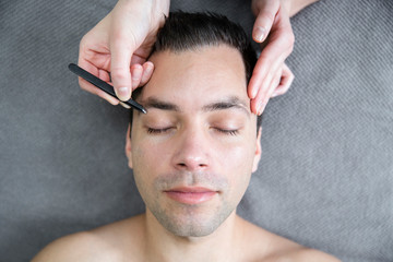 Fototapeta premium Man getting his eyebrows shaped with a tweezer. Beauty skin care for men. 