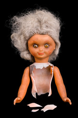 Old broken doll. Isolated on black background. Single damaged toy. Part of dirty child dolly. Gray...