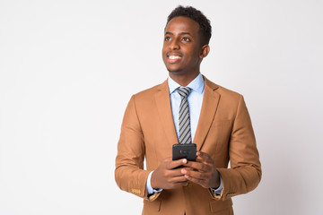 Portrait of young happy African businessman thinking while using phone