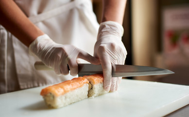 Closeup view of process of preparing rolling sushi. Chef is cutting roll on the white board