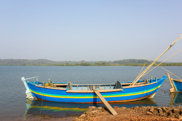 Fototapeta na wymiar blue large fishing boat anchored near the shore against the backdrop of the river and green forest