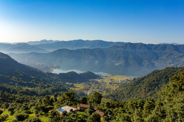 house on a hill against the background of the city of Pokhara in a mountain foggy morning valley with Phewa lake under a clear blue sky