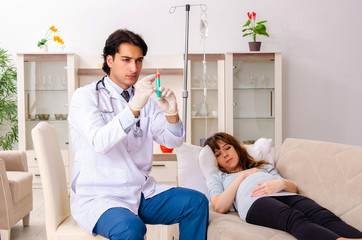 Young handsome doctor visiting pregnant woman at home 