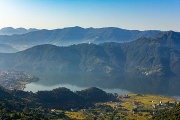 Phewa lake and Pokhara town in a green mountain valley with fog. Aerial view.