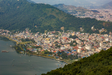 view of the city of Pokhara near the lake Phewa with boats on the water, against the background of the city of the green mountain valley aerial view
