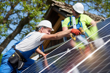 Two workers technicians installing heavy solar photo voltaic panels to high steel platform. Exterior solar system installation, alternative renewable green energy generation concept.