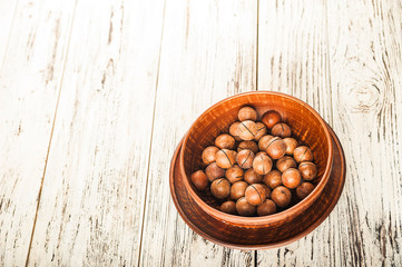 Macadamia nuts on a wooden plate on a white textural table close up and copy space