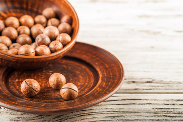Macadamia nuts on a wooden plate on a white textural table close up and copy space