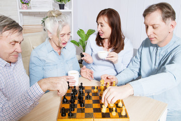 Happy family chess game time at nursing home for elderly. Parents with children have fun talk and leisure. Senior couple and relatives. Visit old mother father. Parenting care concept. Selective focus