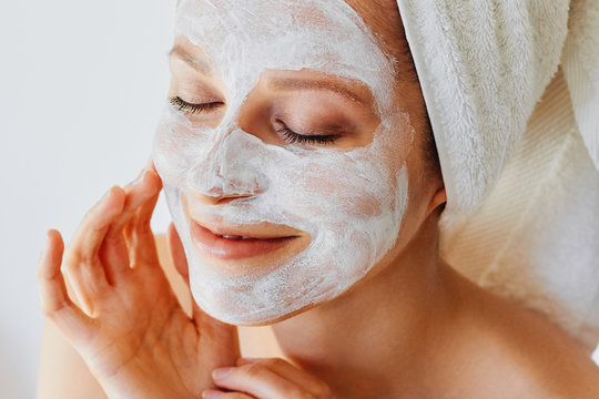 Beautiful young woman with facial mask on her face. Skin care and treatment, spa, natural beauty and cosmetology concept.