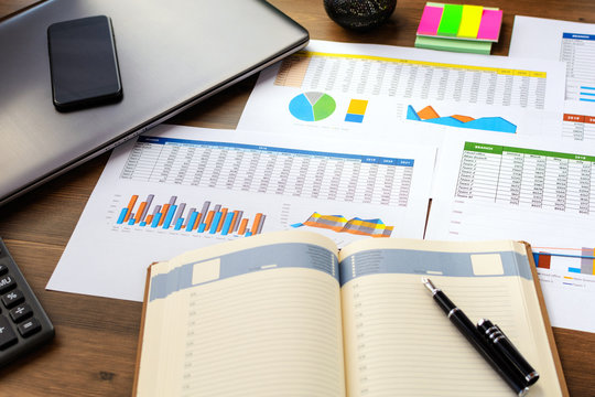 Open leather notebook, drawings, charts, phone, calculator, pencil and laptop on the desk in the office. Business and Finance.