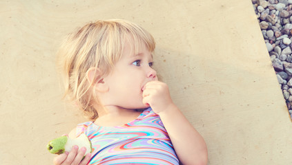 Cute adorable toddler girl eating fresh pear lying on the beach.
