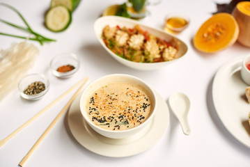 Close up view of tasty dinner for one on white tablecloth. Oriental dinner from soup with seeds, tempura shrimps and noodles with vegetables preparing for client.