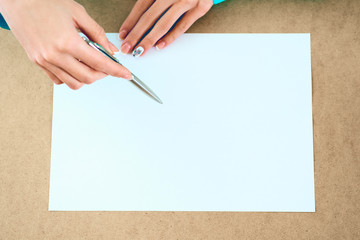 Blank paper lying on the table and waiting for idea with woman's hands over it .