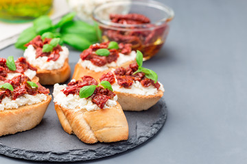 Bruschetta with sun dried tomato, feta and philadelphia cheese and basil on stone plate, horizontal, copy space