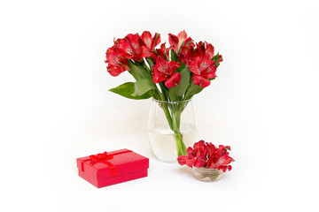 A small bouquet of red flowers Alstroemeria on a white background. A red gift is near the flowers. Content for the celebration of the Eighth of March, Women's Day, Valentine's Day, Birthday.