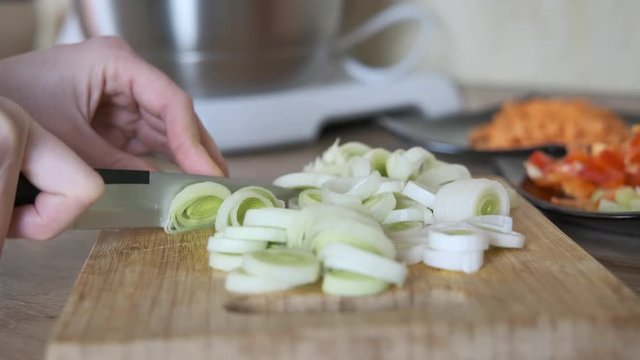 Slicing onions. Women's hands cut leeks on a cutting board.