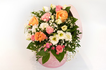 A large beautiful bouquet of pink and orange roses, gypsophila and white flowers in a pink round box with a lid on a white background. Content of holidays, Birthday, Valentine's Day, Women's Day.