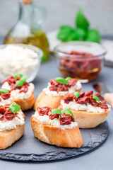 Bruschetta with sun dried tomato, feta and philadelphia cheese and basil on stone plate, vertical, closeup