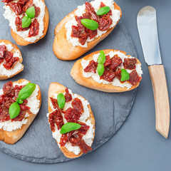 Bruschetta with sun dried tomato, feta and philadelphia cheese and basil on a stone plate, top view, square format, closeup