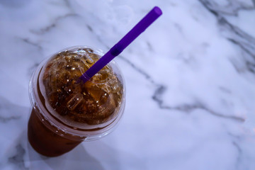 Close up of Cold brew ice-coffee or black tea with straw on blurred background, Selective focus. Cold drink beverage with disposable glass or plastic cup on marble table in cafe restaurant, free space