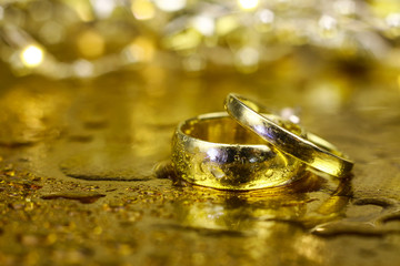 Different size golden marriage rings for men and women. The jewelry covered with water drops on the golden background.