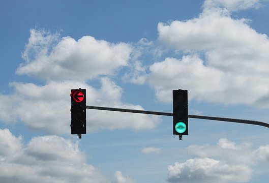 two traffic lights one red to the left side and one green light to driving forward or right with a cloudy sky in the background
