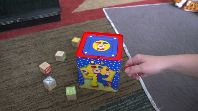 A woman's hand winding a jack-in-the-box toy until it pops up. Shot in slow motion