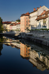 Fototapeta premium Bright buildings at the Ribja Brv modern footbridge reflected in the calm Ljubljanica river canal in Ljubljana Slovenia