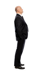 Bald middle-aged man in a suit looks up, full-length, side view. Isolated on white background, vertical.