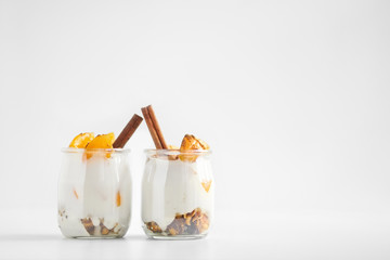 jars of greek yogurt with granola, cinnamon and canned apricots on white background