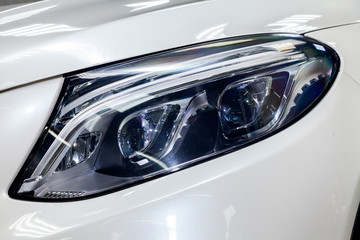 Front led headlamp view in the form of blue eyes of luxury very expensive new white car stands in the washing box waiting for repair in auto service © Aleksandr Kondratov