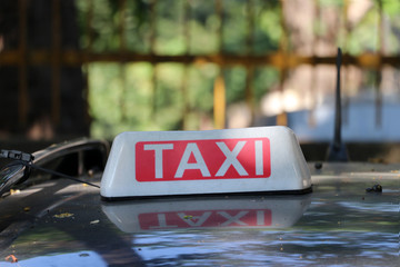 Taxi light sign or cab sign in white and red color with white text on the car roof at blurred background