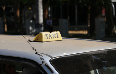 Broken taxi light sign or cab sign in drab yellow color with black text on the car roof at the street blurred background.
