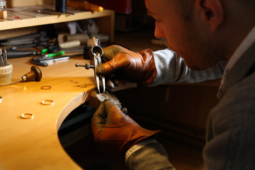 Jeweler measuring a ring with compass divider in a workshop lith with warm light