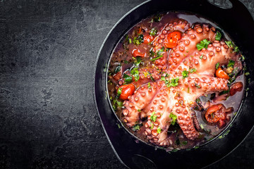 Traditional Greek octopus braised cooked with tomatoes and herbs in ouzo sauce as top view in a...