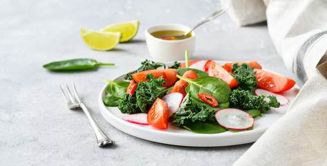 fresh salad of organic spinach, kale, red tomatoes and radish with olive oil and lime juice. healthy eating concept. diet, vegan cuisine. light background, selective focus